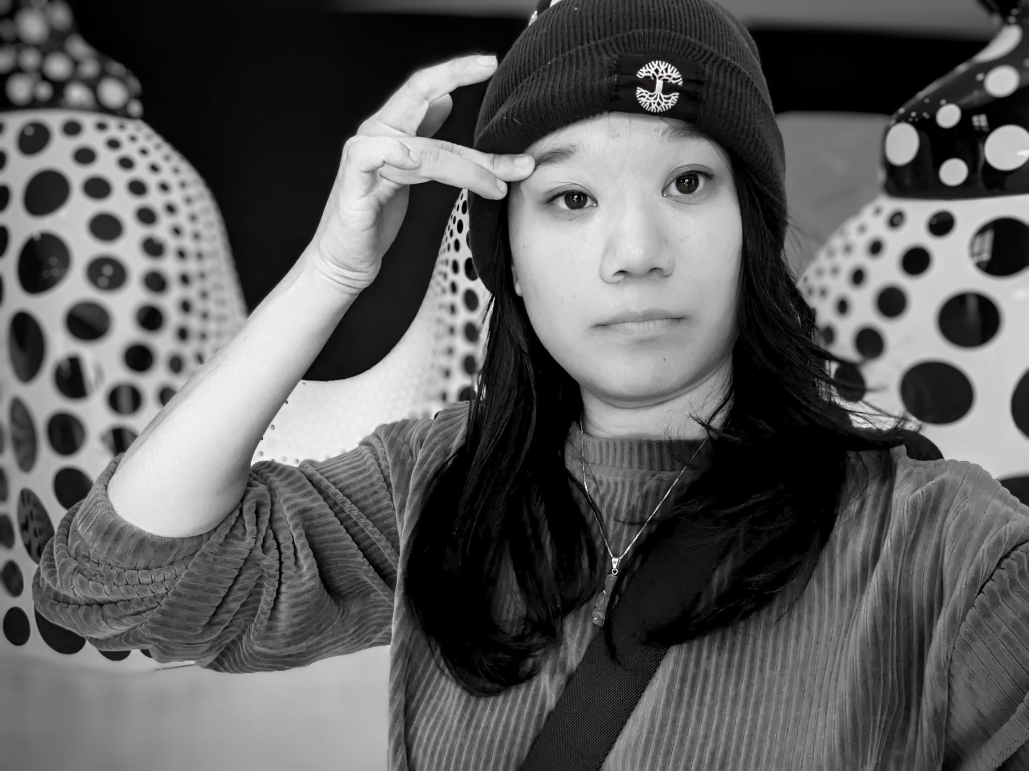 A woman in an Oaklandish beanie wipes her eyebrow in front of Yayoi Kusama's pumpkin sculptures at SFMoma.